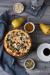 Autumn homemade pear pie with pumpkin seeds and almond petals on wood grey table and coffee cup top view