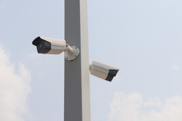two closed-circuit television on white pole against sky background