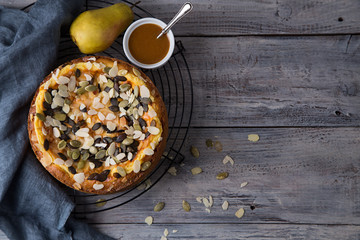 Autumn pear pie with pumpkin seeds and almond petals on blue grey wooden table with caramel, top...
