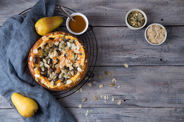 Autumn pear pie with pumpkin seeds and almond petals on blue grey wooden table with caramel, top view