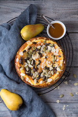 Autumn pear pie with pumpkin seeds and almond petals on blue grey wooden table with caramel, top view