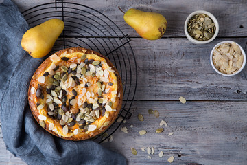 Autumn pear pie with pumpkin seeds and almond petals on blue grey wooden table, top view