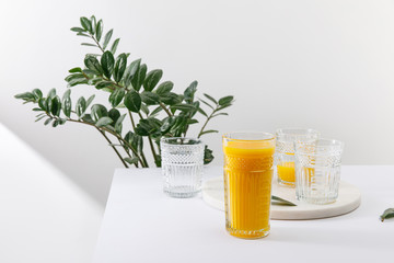 glass of delicious yellow smoothie on white surface near green plant