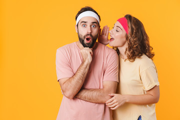 Portrait of athletic couple wondering while whispering secret or gossip