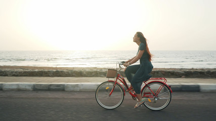 Fototapeta na wymiar Red hair female in green dress ride vintage bicycle along coast line