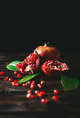 Fresh pomegranate fruits as whole and cut on a rustic wooden background.