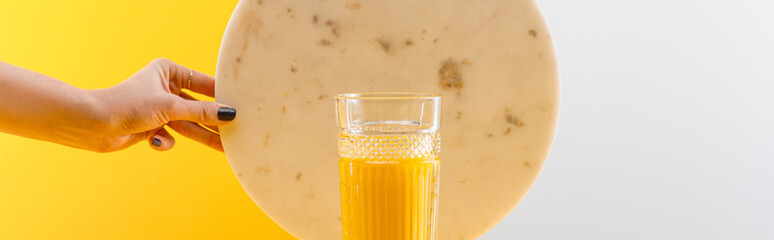 cropped view of woman holding marble circle near glass of fresh delicious yellow smoothie on grey...