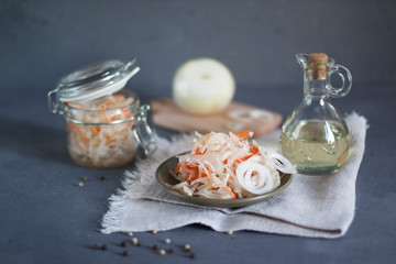 Obraz na płótnie Canvas Shredded cabbage fermented in brine.sauerkraut with carrots and white onions on a plate, a bottle of vegetable oil on a textile napkin, white onions cut on a wooden Board. horizontal orientation