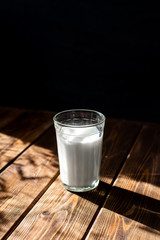 glass of milk on a wooden table. dark background, bright contrasting sun