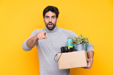 Young handsome man with beard making a move while picking up a box full of things over isolated...