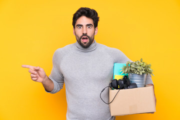 Young handsome man with beard making a move while picking up a box full of things over isolated...