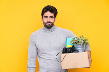 Young handsome man with beard making a move while picking up a box full of things over isolated...