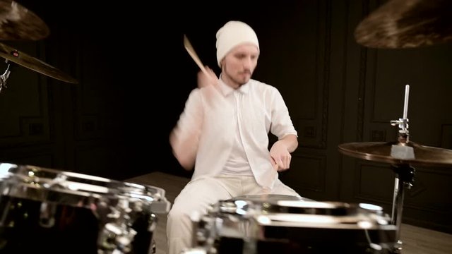 Handsome guy in white actively plays on drum kit in on black background. Closeup
