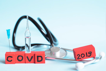 Red cubes with COVD text, a stethoscope and an ampoule on blue background. Defeating coronavirus...