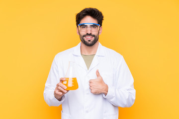 Young scientific man over isolated yellow background with thumbs up because something good has happened