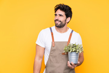 Gardener man with beard over isolated yellow background laughing and looking up