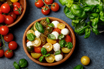 Italian caprese salad with sliced tomatoes, mozzarella cheese, basil, olive oil in wooden bowl. Italian food