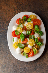 Italian caprese salad with sliced tomatoes, mozzarella cheese, basil, olive oil in wooden bowl. Italian food