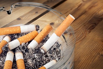 Ashtray and smoked cigarettes with smoke on desk