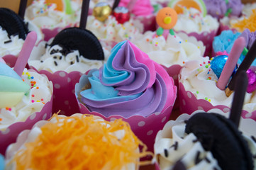 The cup cake a beautiful color in the middle of the picture and there are blurry images of the various cup cakes around.