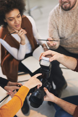 Multicultural attendees of photography class sitting in studio, listening and asking questions about camera parts.