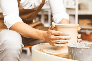 A young male potter works in his workshop on a potter's wheel and makes clay products. Close-up of hands