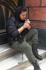 Young photographer smokes a cigarette on his break - obrazy, fototapety, plakaty