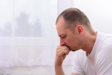 Lonely depressed man near window at home. Unhappy male Isolated on white background. Miserable Caucasian middle aged man at home.