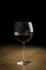 Red wine on a wineglass on a wooden surface isolated on a black background