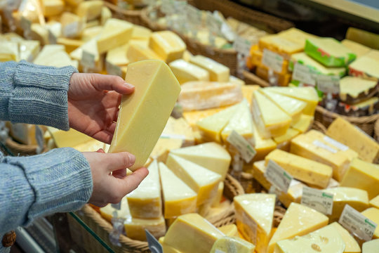 Man shopping cheese in grocery store. Cheese in hands of buyer on background of a large selection of cheeses.