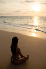 Fototapeta na wymiar beautiful girl yoga coach sitting near the sea and meditating looking at the setting sun in Thailand