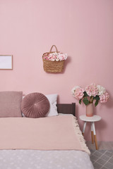 Interior bedroom furniture concept. Cozy Pink Bedroom corner. Cozy, feminine bedroom with pink bed, decorative cushions and plant on a wooden stool. Beautiful and bright bedroom loft style.