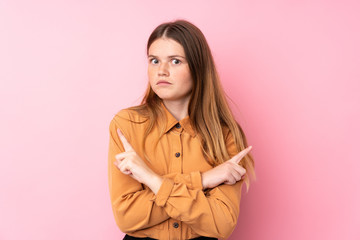 Ukrainian teenager girl over isolated pink background pointing to the laterals having doubts