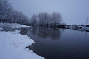 River in winter and tree branches covered with white frost.