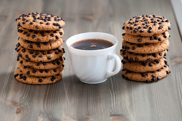 A stack of chocolate chip cookies around coffee cup on a wooden table