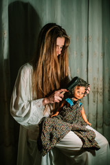 Girl in night gown combing old dolls hair. Bizarre, disturbing concept