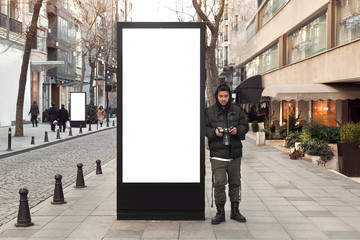 Young photographer stands in front of an empty billboard while taking pictures on the street - obrazy, fototapety, plakaty