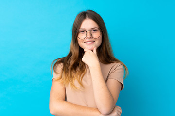 Ukrainian teenager girl over isolated blue background with glasses and smiling