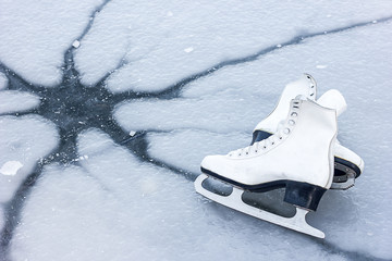  White figure skates lie on ice with a crack, cracked ice. The concept of the danger of being near...
