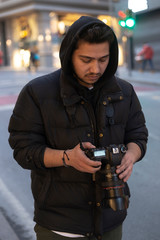 Young photographer looking at his photos on the street - obrazy, fototapety, plakaty