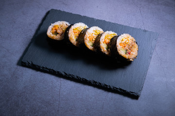 Korean Kimbap with pork and vegetables on slate plate and concrete background. Tradicional cuisine.