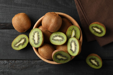 Bowl with ripe kiwi on wooden background, top view