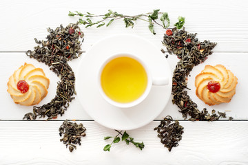 A cup of green tea on white boards. View from above. Composition with a cup of herbal tea and cookies. Creative layout of the herb, green, black teas in the white docks.