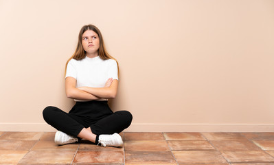 Ukrainian teenager girl sitting on the floor making doubts gesture while lifting the shoulders