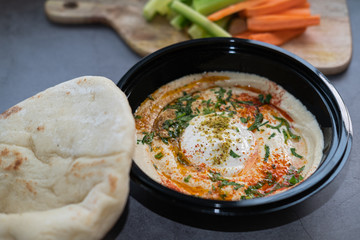 Chickpeas hummus with tahini, paprika, parsley and olive oil on a black plate. Pita bread, carrot and cucumber as side dish. Vegan food. Close up view.