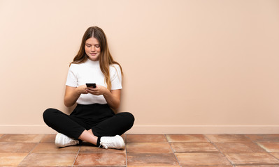 Ukrainian teenager girl sitting on the floor sending a message with the mobile