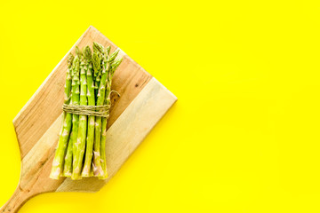 Cooking asparagus. Bunch steams on cutting board on yellow background top-down copy space