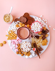 Hot chocolate, marshmallows, chocolates and cookies charcuterie board on pink background