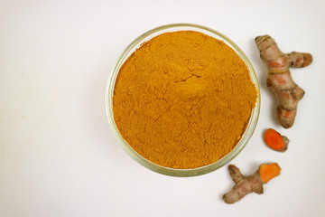 Turmeric powder in a glass cup and turmeric root extracted on a white background, used as a tonic for the body and food ingredients.