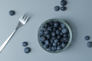 Delicious transparent glass bowl of fresh organic blueberries and a fork on a modern kitchen countertop
